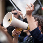 Unidentified young demostrator with megaphone and notebook protesting against austerity cuts