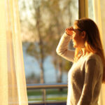 Side view portrait of a happy teenage girl scouting through a window at home